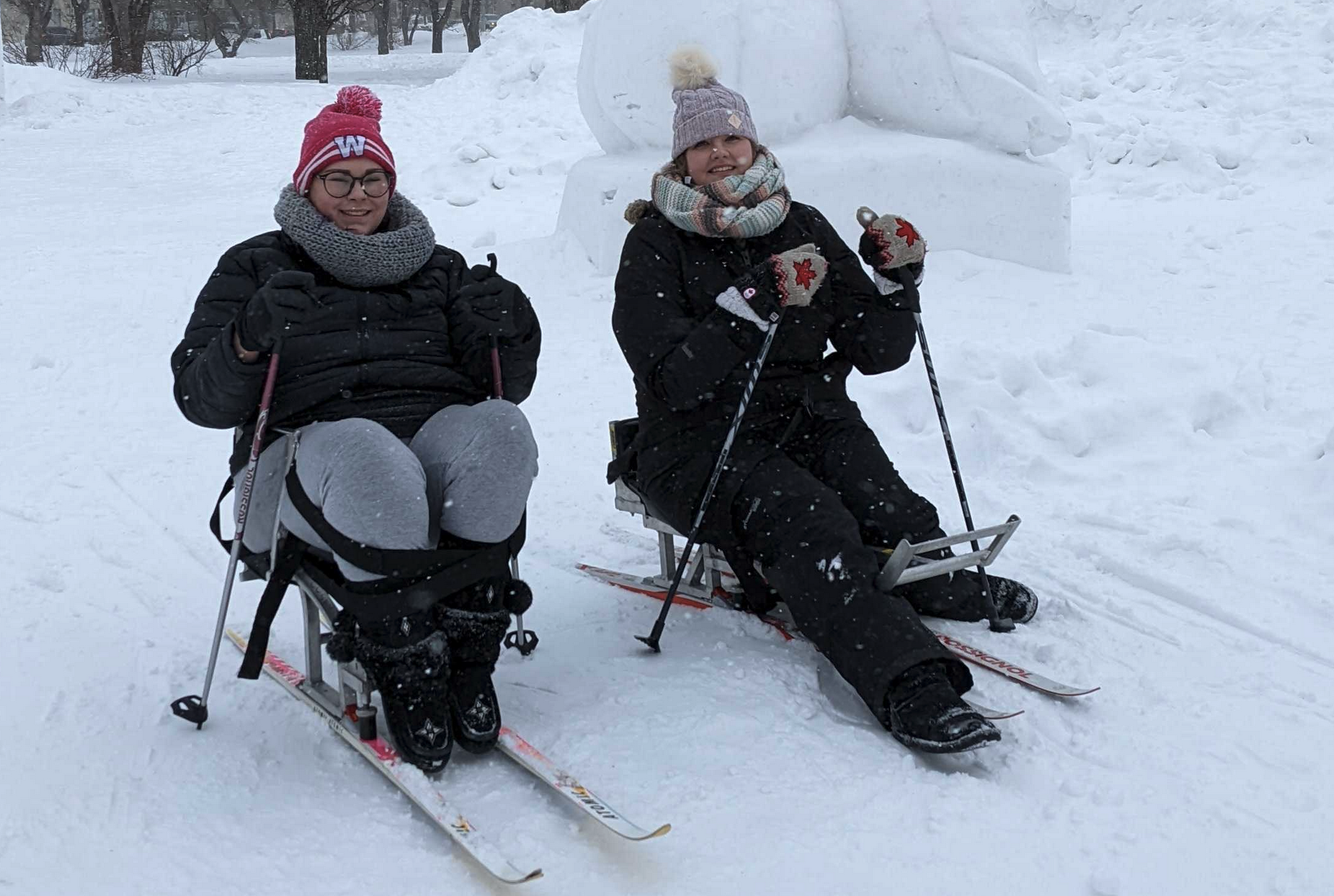 Two smiling women in a wintry landscape on sit skis.